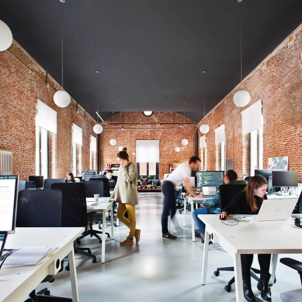 Spacious office to rent on Calle Vandergoten 1, Madrid Retiro, showcasing an open, brick-walled workspace with individuals actively working at desks.