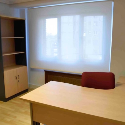 Bright office space with wooden desks and an empty bookshelf at Calle Capitan Haya 60, ideal for office space rental in Madrid Tetuán.