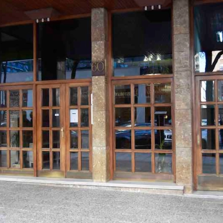 Exterior view of the office building at Calle Capitan Haya 60, Madrid Tetuán, showcasing large wooden doors and street reflections, ideal for office space rental.