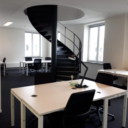 Modern office space with spiral staircase at Kardinaal Mercierplein 2 in Mechelen Centrum, available for rent. Features multiple desks and chairs, creating an inviting workspace atmosphere.