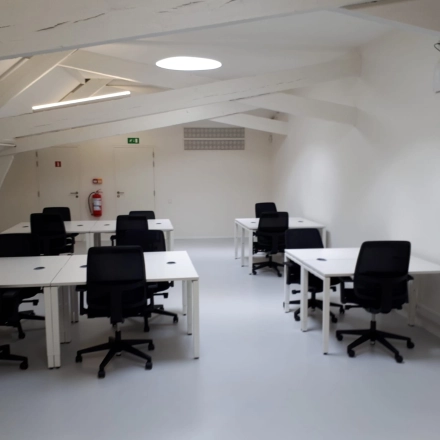 Bright office space available for rent in Mechelen Centrum, featuring black chairs and white desks under modern lighting.