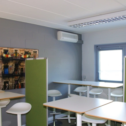 Furnished office space rental at De Regenboog 11 in Mechelen North with white tables, green dividers, and tall chairs under bright lighting.