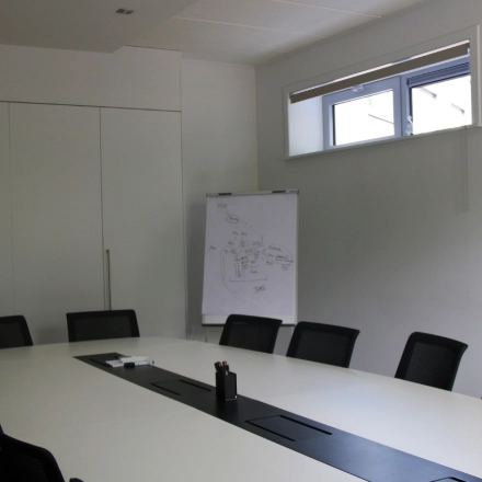 Conference room with a long white table, black chairs, and a flip chart in an office for rent at De Regenboog 11, Mechelen North.