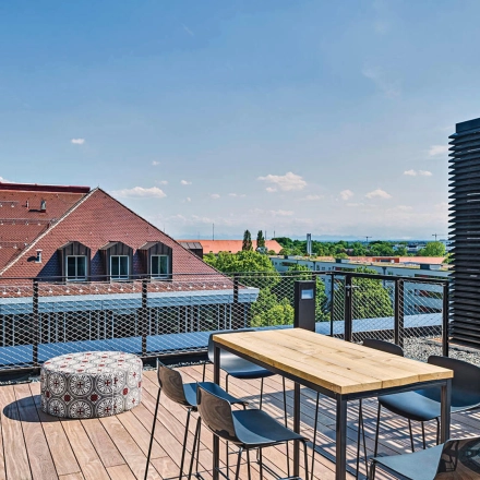 Outdoor office space in München Werksviertel with a wooden deck, table, and chairs offering a panoramic view of the surrounding rooftops and distant horizon.
