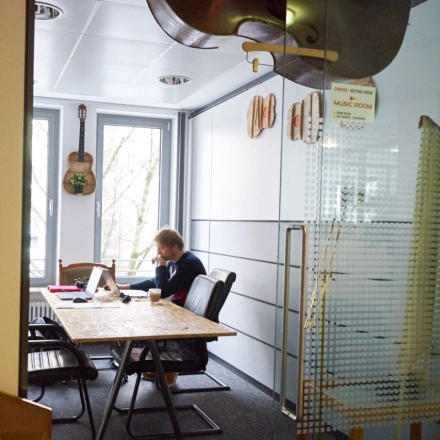Cozy office space with a person working at a desk, decorated with wall-mounted guitars. Ideal for office space rental in Munich Giesing.