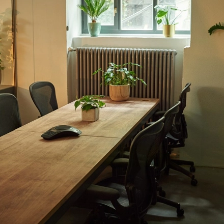 Cozy office space at Amalienstraße 71, Munich Maxvorstadt, featuring a wooden conference table surrounded by chairs, accented with potted plants for a refreshing touch. Ideal for office space rental.