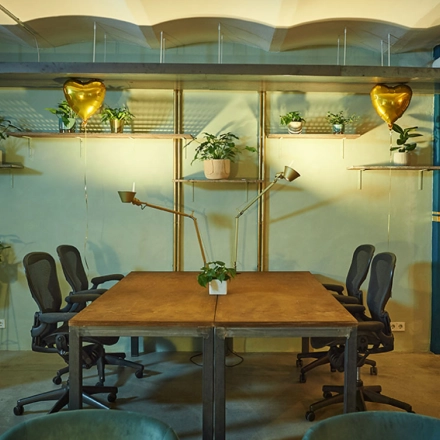 Furnished interior of a cozy office for rent at Amalienstraße 71, Munich Maxvorstadt, featuring wooden tables, chairs, decorative plants, and warm lighting, ideal for workspace and office space rental.