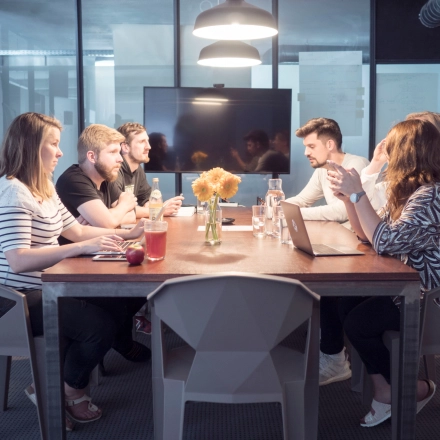 People collaborating in a furnished office space with a large table and modern decor. Ideal for rent office space in Munich Maxvorstadt.