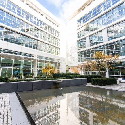 Exterior view of a modern office building at Oskar-von-Miller-Ring 20, Munich Maxvorstadt, featuring a courtyard with seating and water feature.