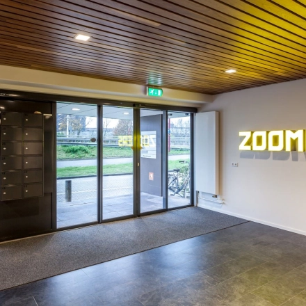 Entrance area at Zoomstede 19 in Nieuwegein, featuring modern glass doors, illuminated signage, and mailbox units, ideal for office space rental.