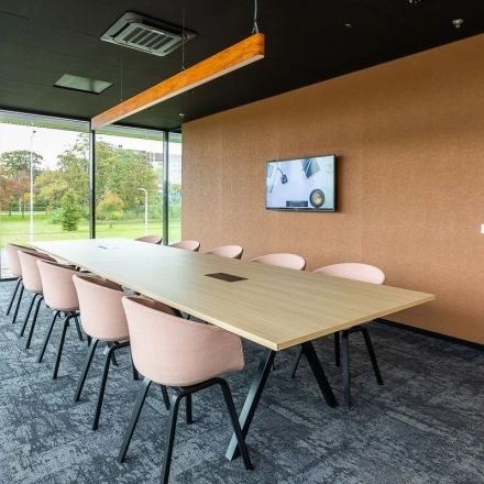 Modern conference room with a long wooden table and pink chairs at Jonkerbosplein 52 in Nijmegen, ideal for office space rental.