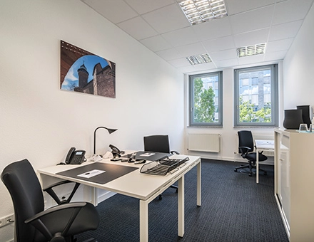 Bright office space with two desks, chairs, and a view of the outside greenery at Südwestpark 67, Nürnberg Röthenbach, perfect for office space rental.