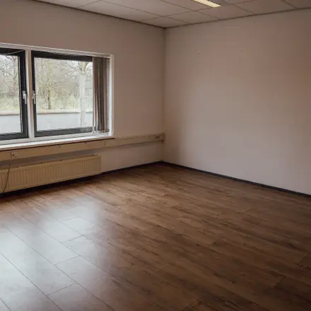 An empty interior space with wooden flooring and a large window, ideal for those seeking office space rental in Oosterhout Nb.