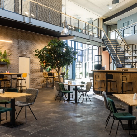 Spacious furnished office for rent at Veengang 1, Oosterwolde. Features open seating areas with plants and a staircase, ideal for office space rental.