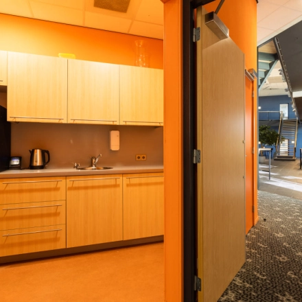 Interior view of a furnished office space with a pantry area, featuring wooden cabinets, a coffee machine, and a kettle. Ideal office space rental opportunity at Veengang 1, Oosterwolde.