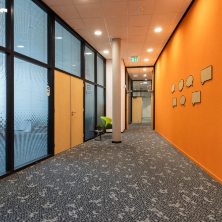 Bright office corridor at Veengang 1, Oosterwolde, ideal for office space rental, featuring vibrant walls and carpeted floors.