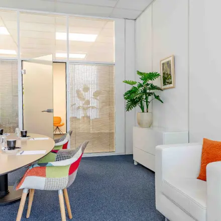 Bright office space with a round meeting table, colorful chairs, and a cozy seating area, ideal for office space rental in Reeuwijk.