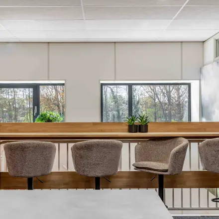Modern office space with bar stools and plants, offering a scenic view through large windows.