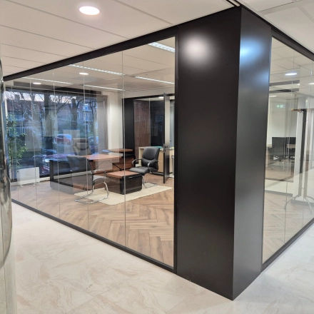 Modern office space rental located at JC van Markenlaan 3, Rijswijk, featuring glass walls, stylish wooden flooring, and contemporary seating arrangements.