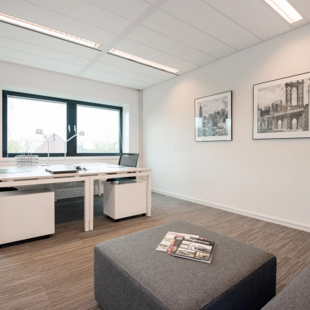 Bright office space with modern furnishings, featuring a large window and artwork on the walls. Ideal for office space rental.