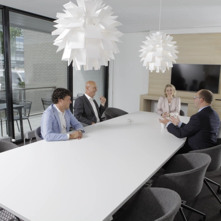 A furnished meeting room in an office space at Laan van Vredenoord 33, Rijswijk, with four people in business attire having a discussion around a white table. Ideal for office space rental.