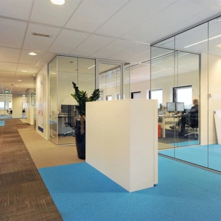 Modern office to rent at Patrijsweg 62, Rijswijk, featuring glass-walled workspaces and a blue carpet. Ideal for office space rental.