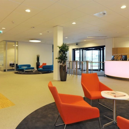 Spacious office reception area at Patrijsweg 62, Rijswijk, featuring modern decor with orange and blue seating and a sleek reception desk. Ideal for those seeking office space rental.