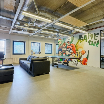 Spacious office to rent with modern furnishings, featuring a playful mural and a ping pong table, situated at Patrijsweg 62, Rijswijk. Ideal office space rental for creative work.