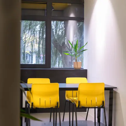 Office space for rent at Volmerlaan 7, Rijswijk, featuring bright yellow chairs around a table with a potted plant against a window backdrop.