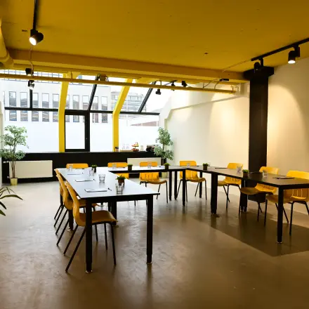 Bright office space at Volmerlaan 7, Rijswijk, featuring yellow accents, large windows, and modular desks, ideal for office space rental. Perfect for dynamic setups in this airy, inviting office to rent.