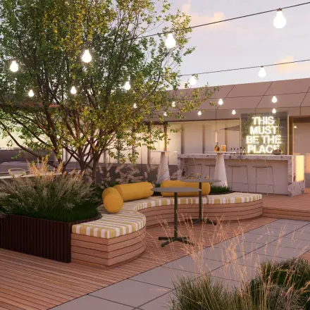 Outdoor rooftop space with wooden benches, plants, and a bar area under string lights, perfect for office space rental in Rotterdam Alexander.