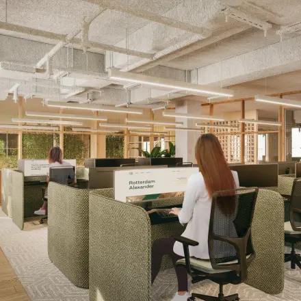 Modern office space for rent in Rotterdam Alexander featuring open workstations with people working on computers. Bright and stylish interior design with natural light and green accents.