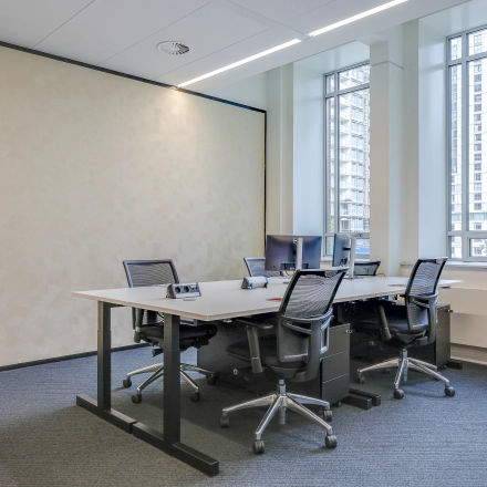 Modern office space rental at Blaak 34, Rotterdam Center, featuring a bright workspace with several desks and chairs by large windows.