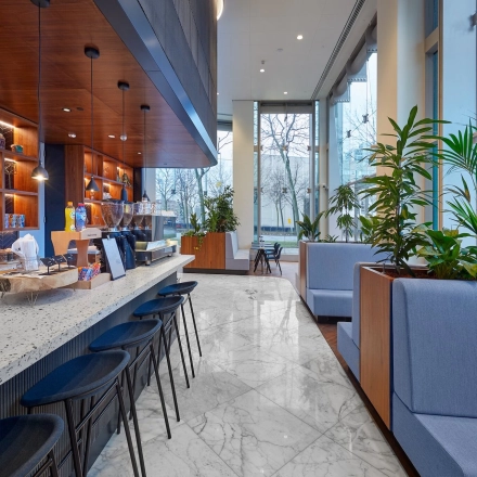 Modern office lounge area at Blaak 555 in Rotterdam Center with stylish seating, plants, and a coffee bar, ideal for office space rental.
