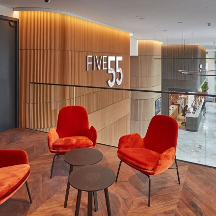 Modern office lounge area at Blaak 555, Rotterdam Center, featuring stylish red chairs and wood paneling. Ideal office space rental opportunity.