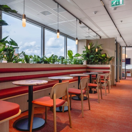 Bright workspaces at Blaak 555 in Rotterdam Center, featuring vibrant red seating and lush plants, available for office space rental.