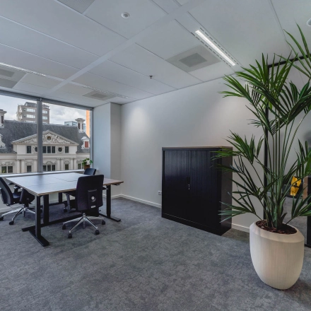 Bright office space with large window view at Blaak 555, Rotterdam Center. Ideal for office space rental with modern furnishings and a potted plant.