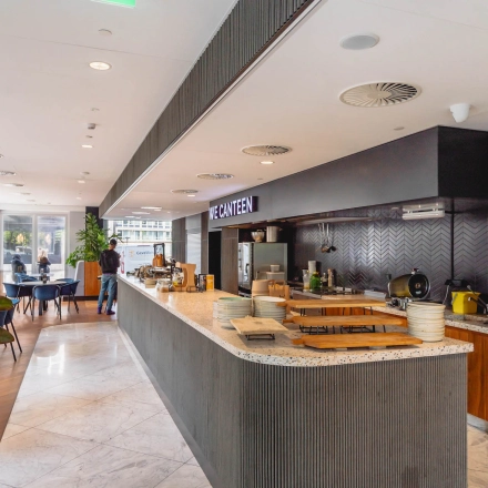 Interior of Blaak 555, Rotterdam Center, featuring a modern canteen area. A person is preparing food at the counter, suitable for office space rental.