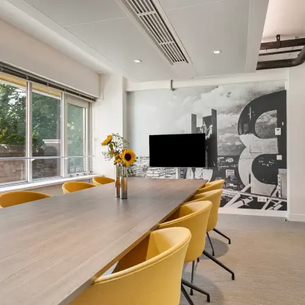 Bright conference room with a long table and yellow chairs, featuring large windows and a modern wall design. Ideal office space rental in Rotterdam Center at Coolsingel 104.
