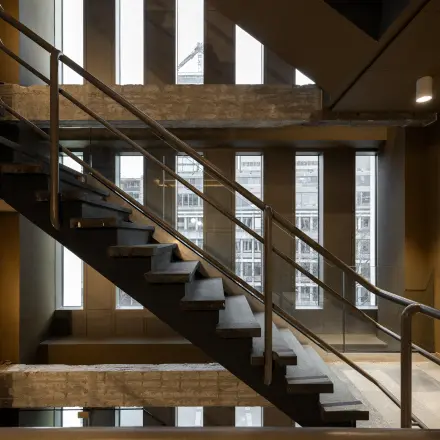 Interior view of a modern office at Stadhuisplein 9-23, Rotterdam Center, featuring industrial-style staircases and windowed walls. Ideal for office space rental.
