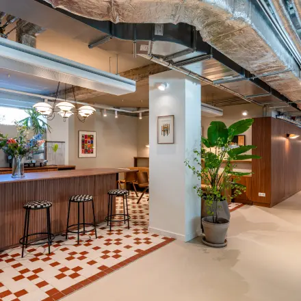Modern office interior in Rotterdam Center with a stylish open floor plan featuring decorative plants, a bar-height table, and stools for collaborative work. Ideal office space rental with flexible options.