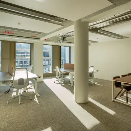 Bright office space with modern furniture and large windows at Stadhuisplein 9-23, Rotterdam Center for rent. Several desks and chairs arranged for business activities, ideal for office space rental.