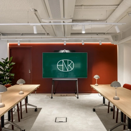 Modern conference room in office space rental at Vasteland 42-110, Rotterdam Center, featuring two long tables, chairs, lamps, and a digital screen.