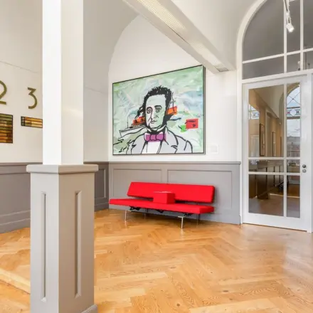A stylish reception area at Veerhaven 7, Rotterdam Center, featuring parquet flooring, a vibrant painting, and a sleek red bench. Ideal space to rent as office or for office space rental.
