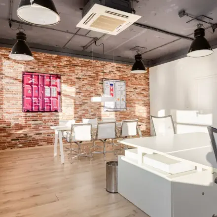 Bright office space at Veerhaven 7, Rotterdam Center with modern decor, featuring white desks, mesh chairs, and industrial lighting against a brick wall, suitable for rental.