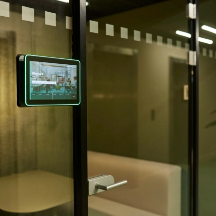 Modern office space rental with glass partitions in Rotterdam Center at Weena 335. A visible meeting room tablet signifies a high-tech workspace ambiance. Ideal for those seeking an office to rent.
