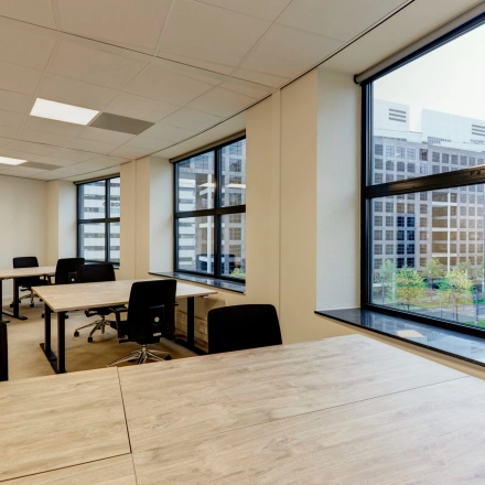 Spacious office space rental with large windows in Rotterdam Center, featuring wooden desks and rolling chairs, ideal for those looking to rent office space at Weena 335.