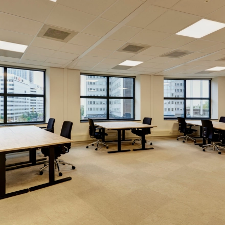 Bright office space at Weena 335, Rotterdam Center, featuring large windows and modern furniture. Ideal for those looking to rent office space with multiple desks and chairs.