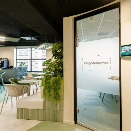Modern office space rental at Weena 335, Rotterdam Center, featuring stylish furniture and a meeting room labeled 'Vergaderkamer'. Decorative plants add a refreshing touch to the open workspace environment.