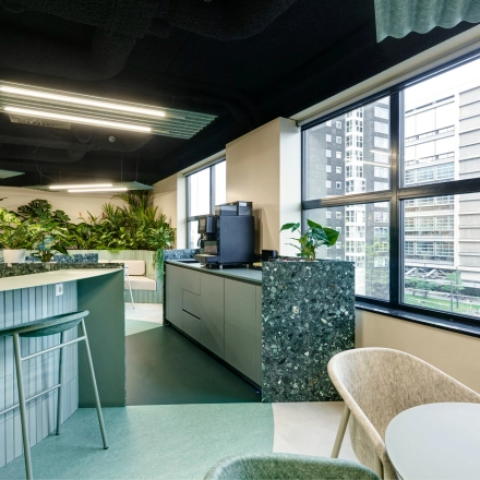 Stylish office space with modern furnishings and lush plants, offering a view of Rotterdam Center. Ideal for office space rental at Weena 335.